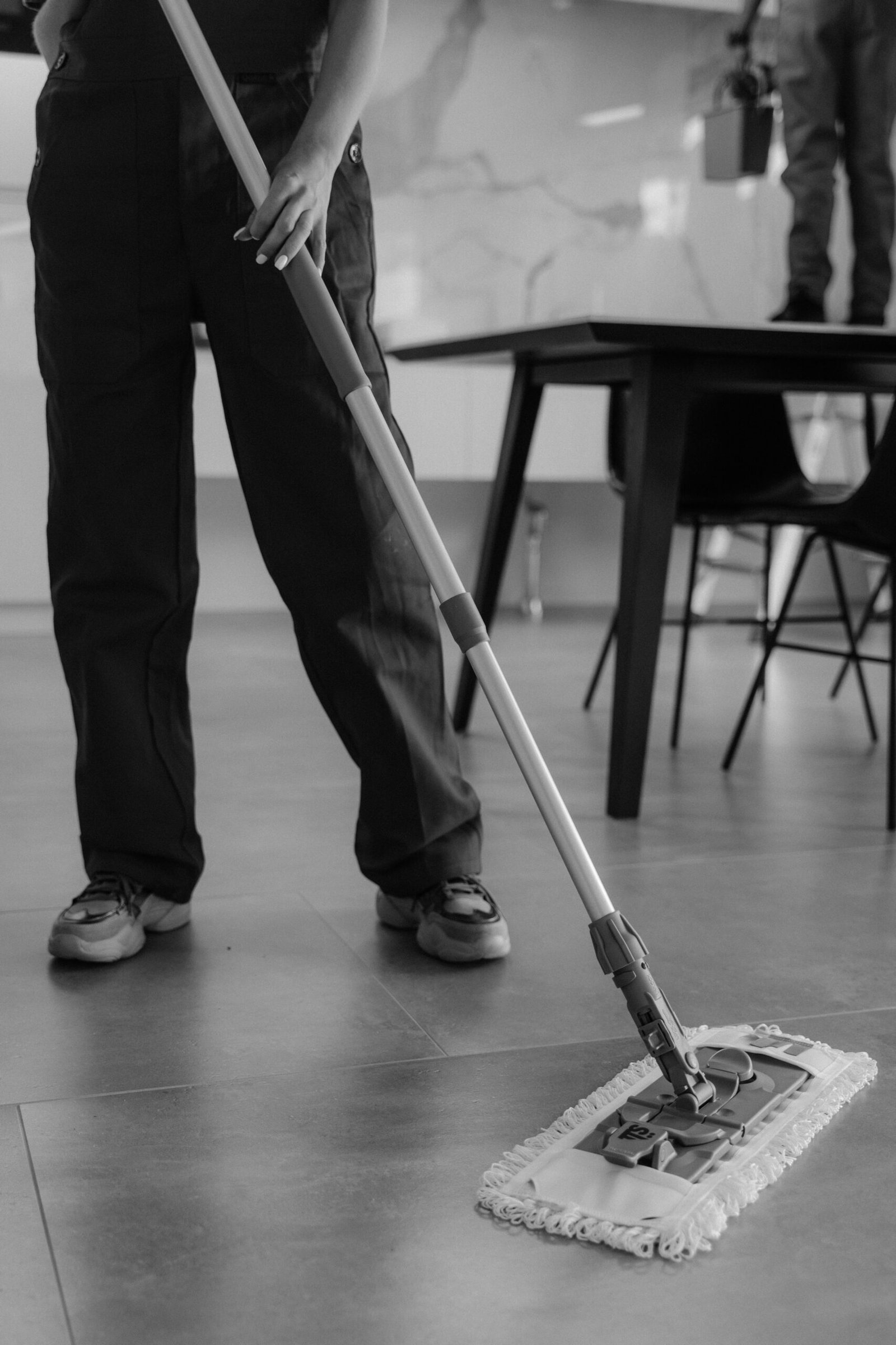 Services Monochrome image of a person mopping a tiled floor in an indoor setting.